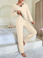 Woman wearing a cream-colored ribbed knit loungewear set with black trim and a black bow, posing on a bed.