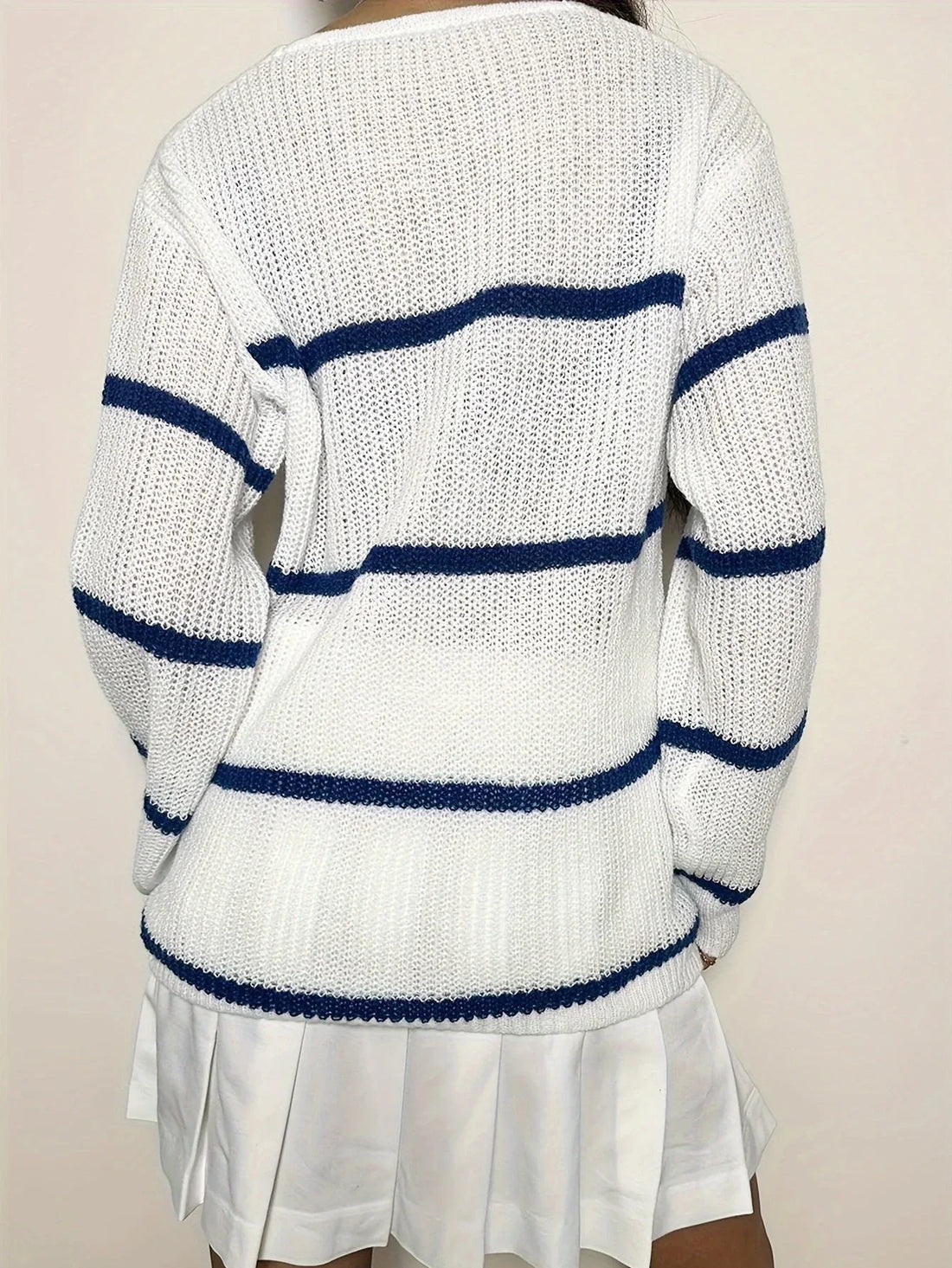 Woman wearing a white knit sweater with horizontal navy blue stripes and a v-neckline.