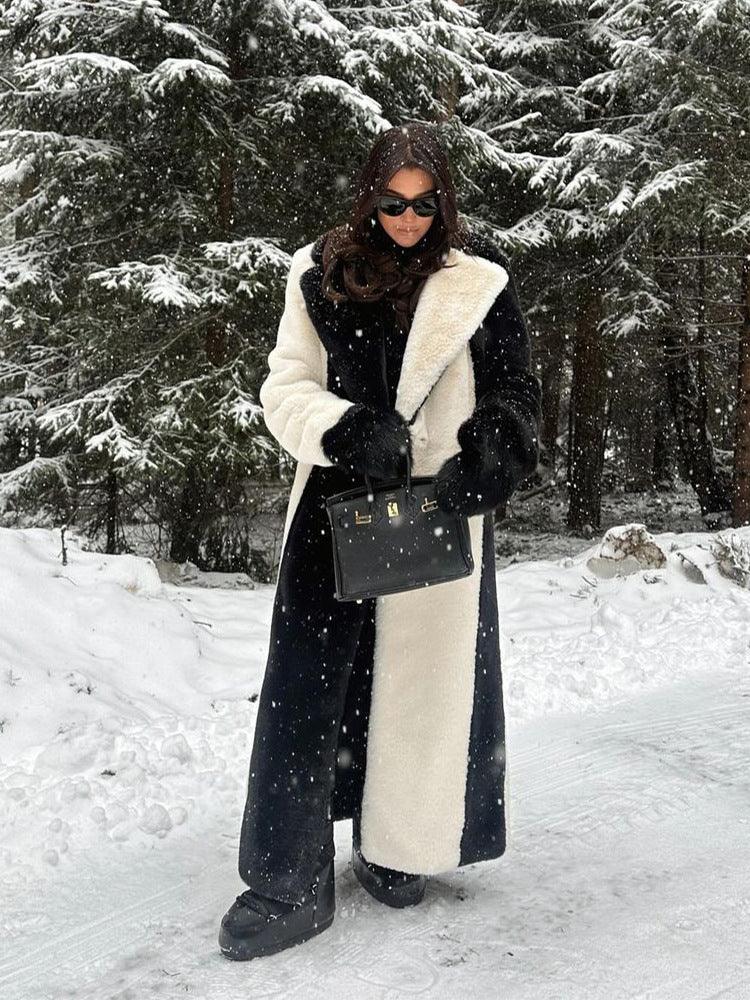 Woman standing in the snow, wearing a long black and white faux fur coat and holding a black handbag.