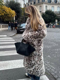 Woman wearing a long leopard print faux fur coat crossing a street in a city.