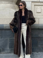 Woman wearing a long, dark brown faux fur coat with wide lapels.