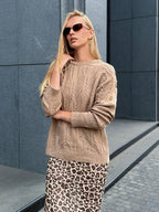 Front view of a woman in a tan textured knit sweater and blue jeans.