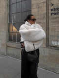 Woman in a white faux fur jacket standing outdoors.