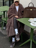 Woman with a brown faux fur coat, sunglasses, and a baseball cap sitting at a table.