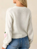 Rear view of a woman wearing a white cropped knit sweater with a strawberry applique on the sleeve, paired with blue denim jeans.
