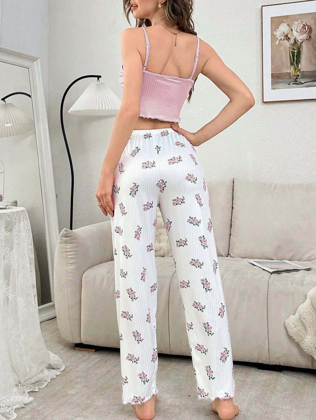 Rear view of a woman in a pink ribbed crop top and white floral print pajama pants standing in a living room.
