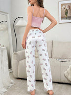 Rear view of a woman in a pink ribbed crop top and white floral print pajama pants standing in a living room.