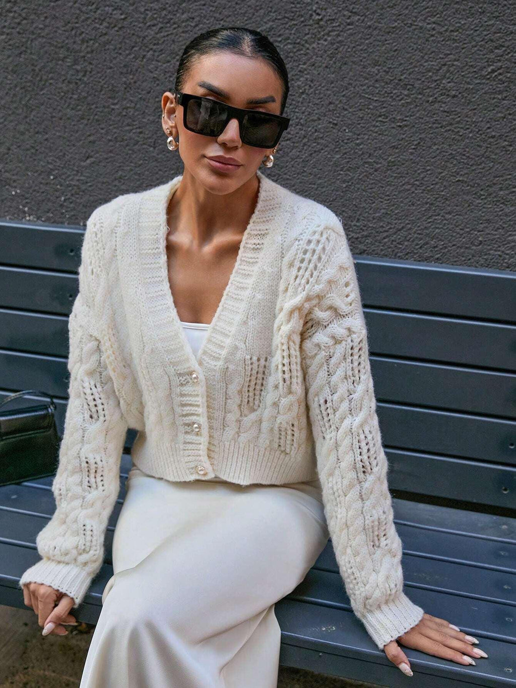 Close-up of a woman wearing a cream cable knit cropped cardigan with pearl buttons and sunglasses.