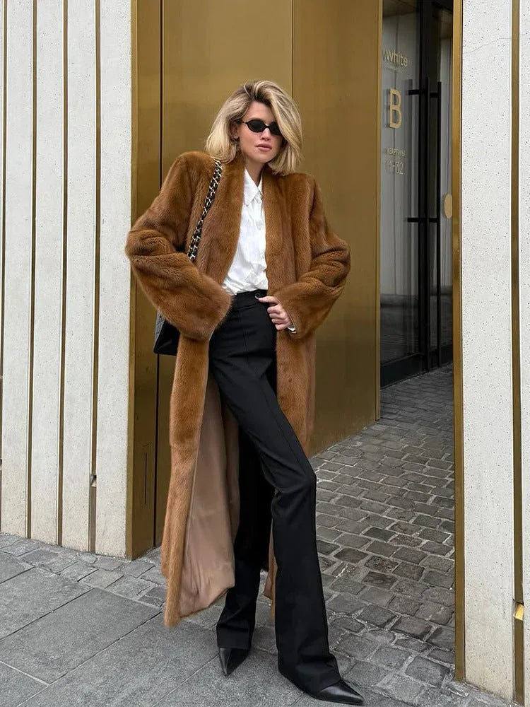 Woman wearing a long brown faux fur coat over a white shirt and black pants. Main image