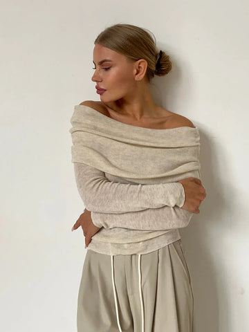Woman wearing a beige off-the-shoulder ribbed knit sweater with a draped cowl neck and long sleeves.
