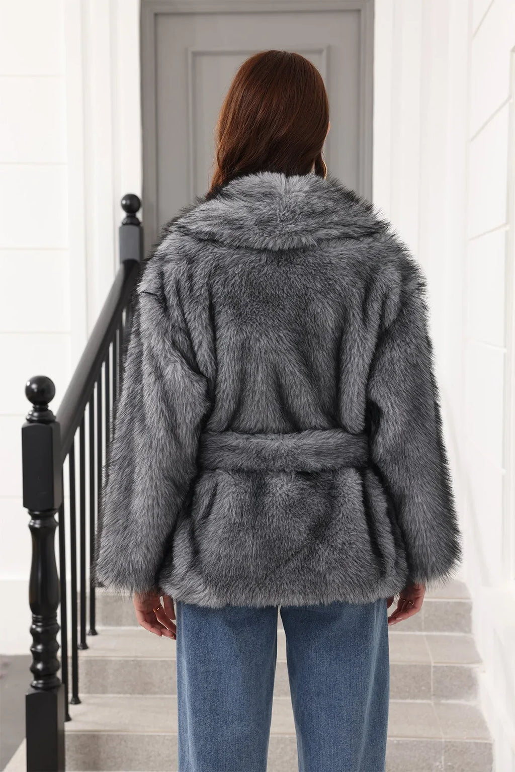 Rear view of a woman in a grey faux fur jacket with a belted waist.