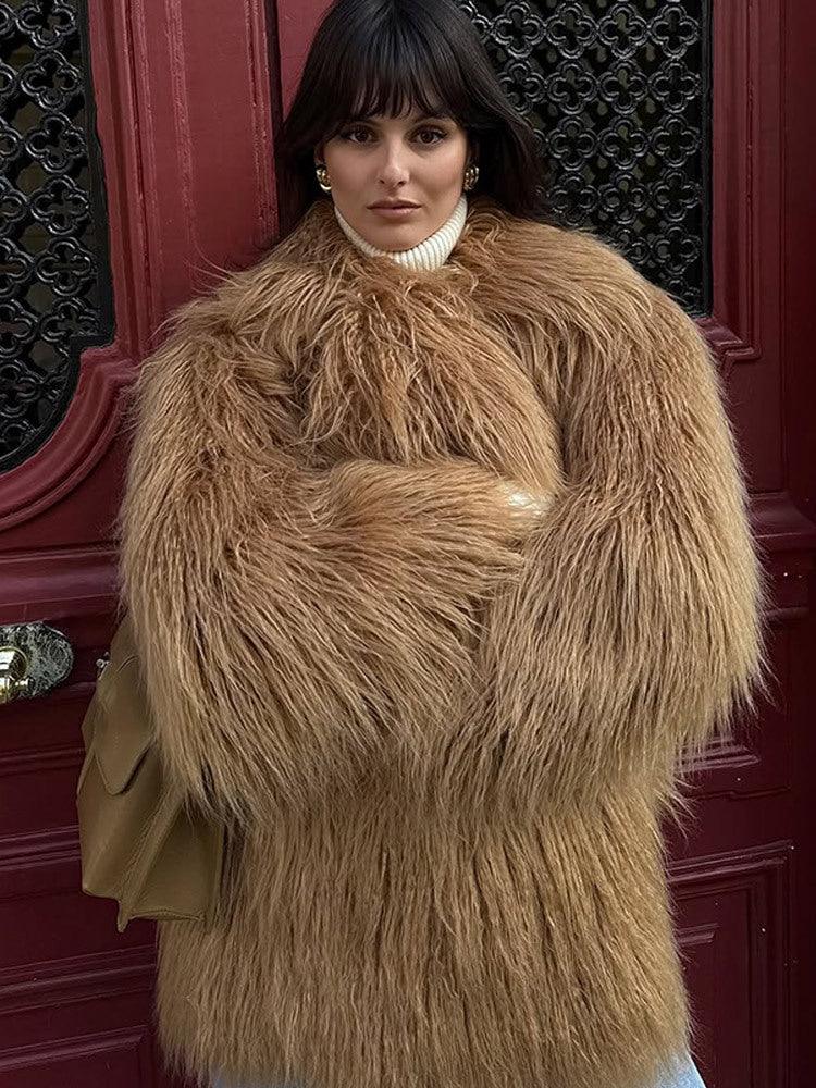 Woman in a tan shaggy faux fur coat and white turtleneck standing in front of a red door