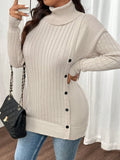 Woman in a cream ribbed knit turtleneck tunic sweater and blue jeans, holding a black quilted handbag.