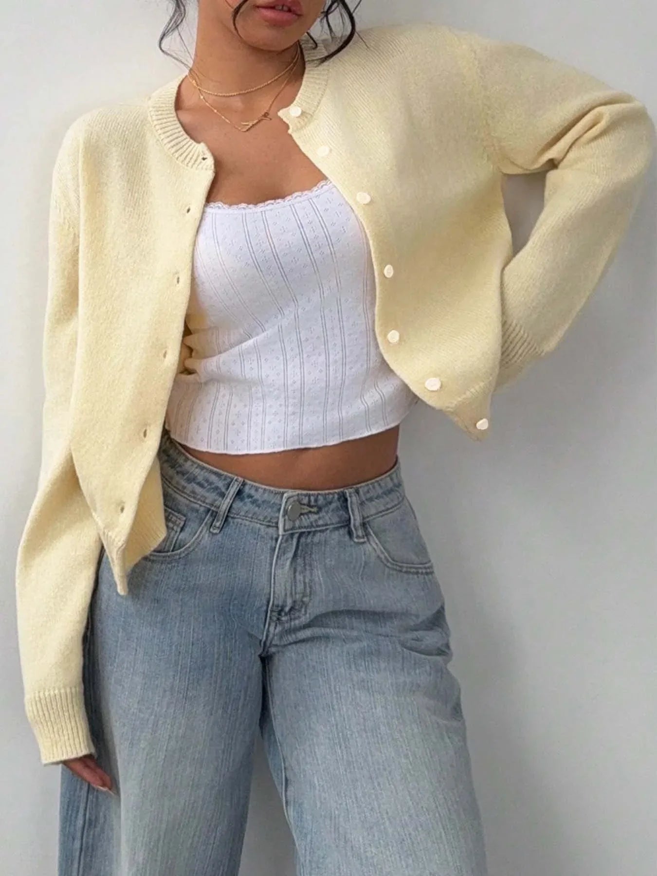 Woman in a yellow cardigan and jeans, leaning against a wall.