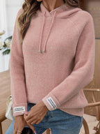 Close-up of a woman's arms wearing a pink hooded knit sweater with label detail