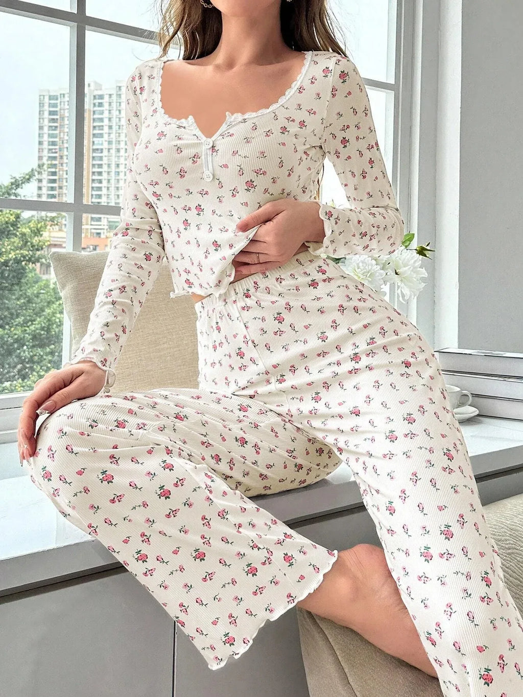 Woman sitting on a windowsill wearing a cream floral print long sleeve pajama set