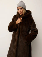 Woman wearing a long brown faux fur coat with a hood and a grey beanie.