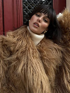 Close-up of a woman wearing a tan shaggy faux fur coat and a white turtleneck
