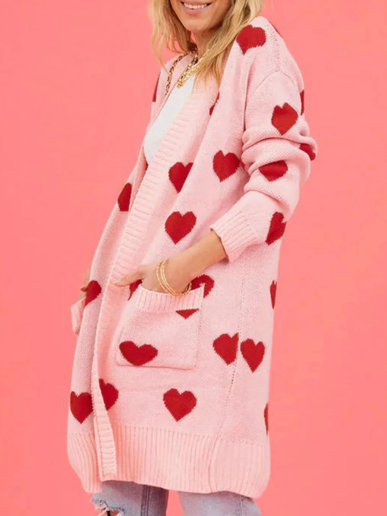 Side profile of a woman with her hands in the pockets of a pink heart print cardigan.