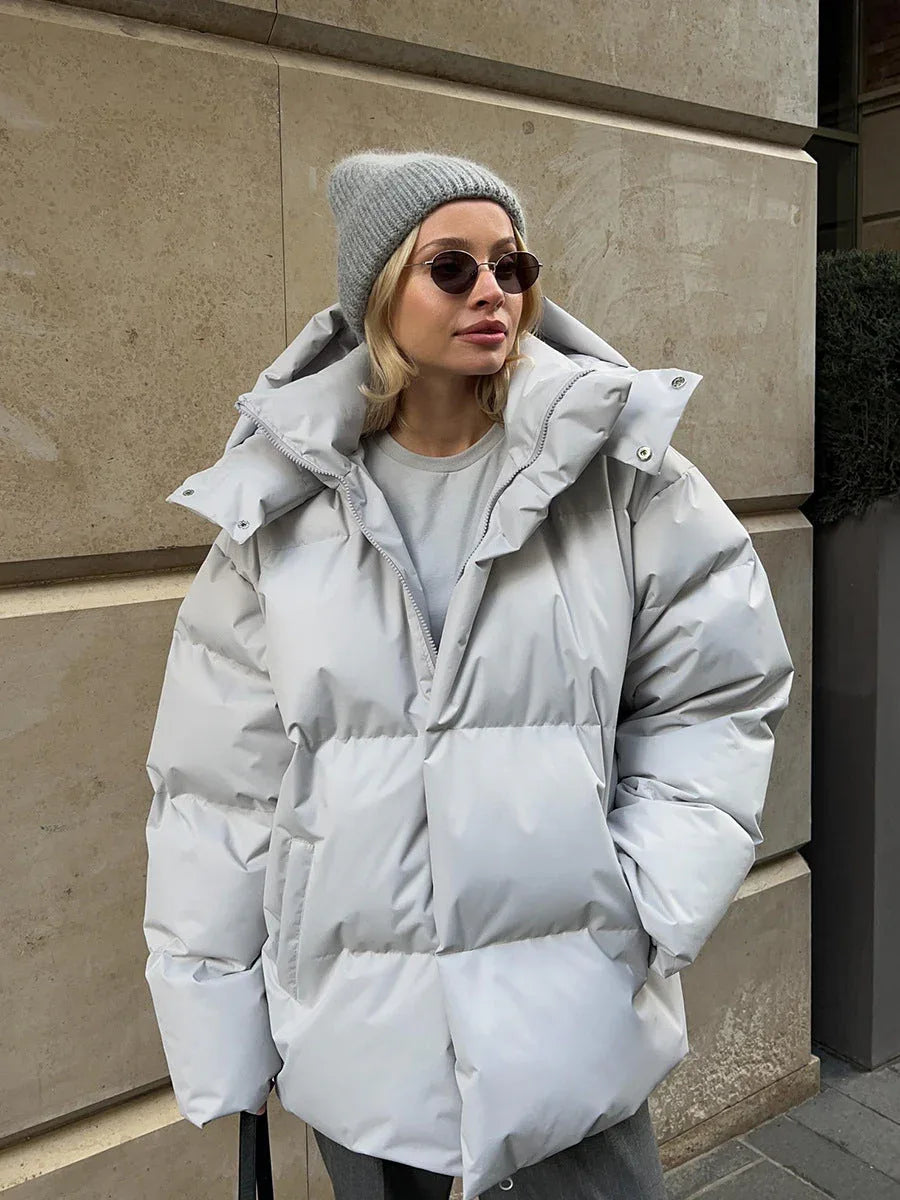 Close-up of a woman wearing a light gray puffer jacket with a large hood.