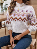 Woman sitting down, wearing a white knit sweater with a geometric pattern and blue jeans.