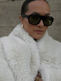 Close-up of a woman wearing a white faux fur jacket and sunglasses.