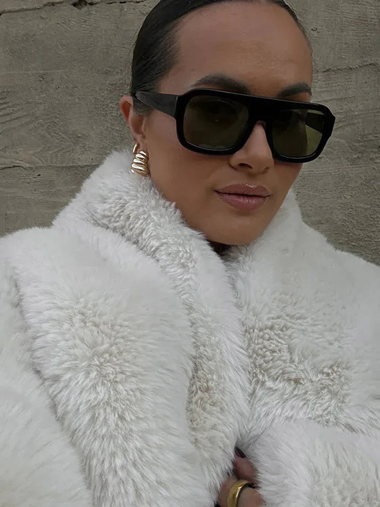 Close-up of a woman wearing a white faux fur jacket and sunglasses.