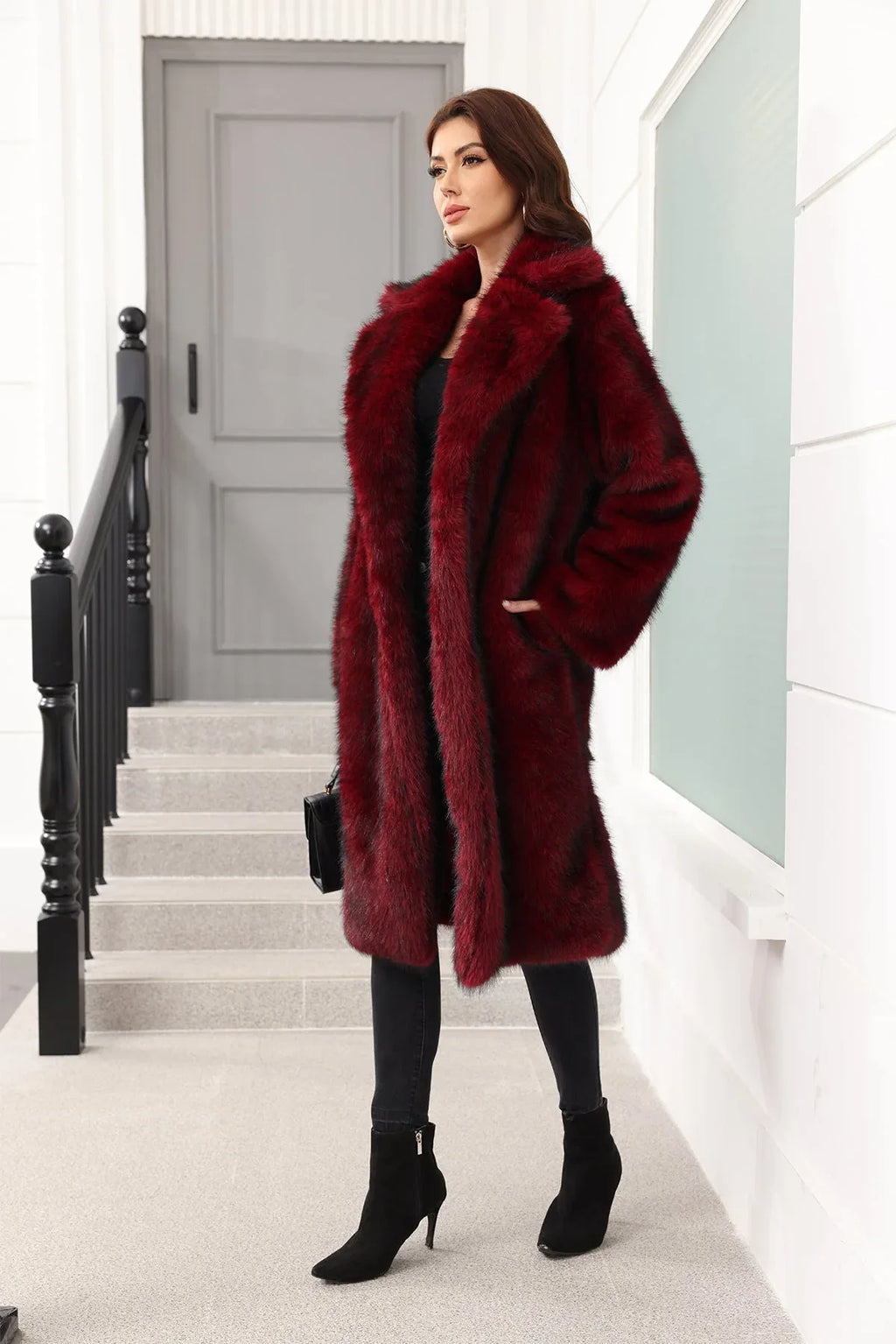 Woman in a dark red faux fur coat, posing with hands in pockets, standing on stairs.