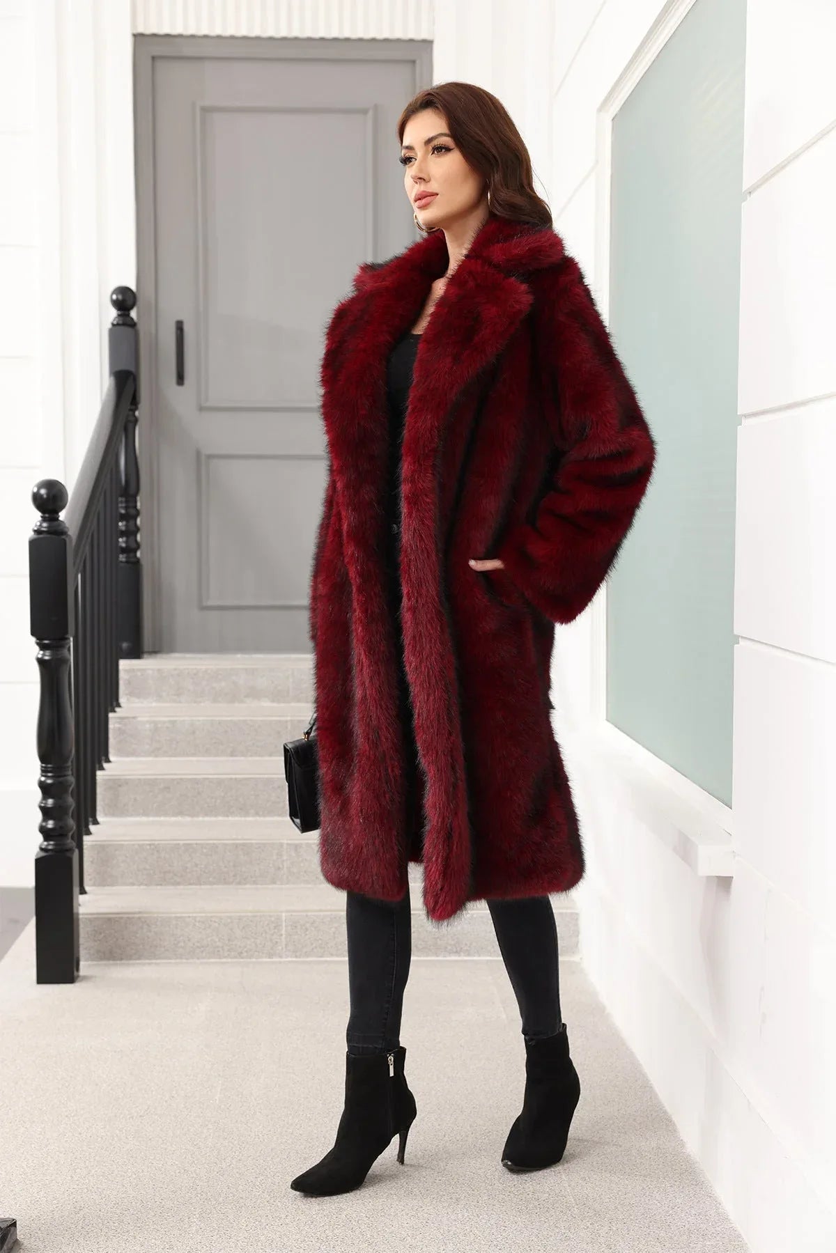 Woman in a dark red faux fur coat, posing with hands in pockets, standing on stairs.
