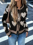 Woman wearing a black knit cardigan with a heart and leopard print pattern, featuring a tie closure and contrast trim.