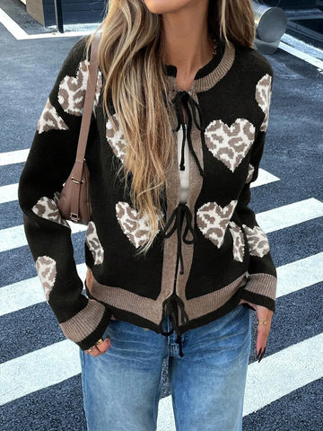 Woman wearing a black knit cardigan with a heart and leopard print pattern, featuring a tie closure and contrast trim.