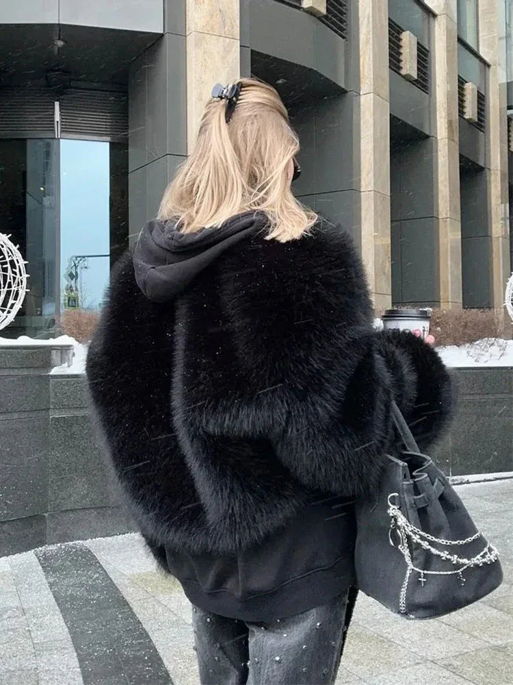 Rear view of a woman wearing a black faux fur bomber jacket over a black hoodie, carrying a black handbag.