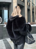 Rear view of a woman wearing a black faux fur bomber jacket over a black hoodie, carrying a black handbag.