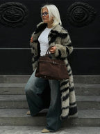 Woman walking down steps wearing a long faux fur coat, jeans, and carrying a brown suede handbag.