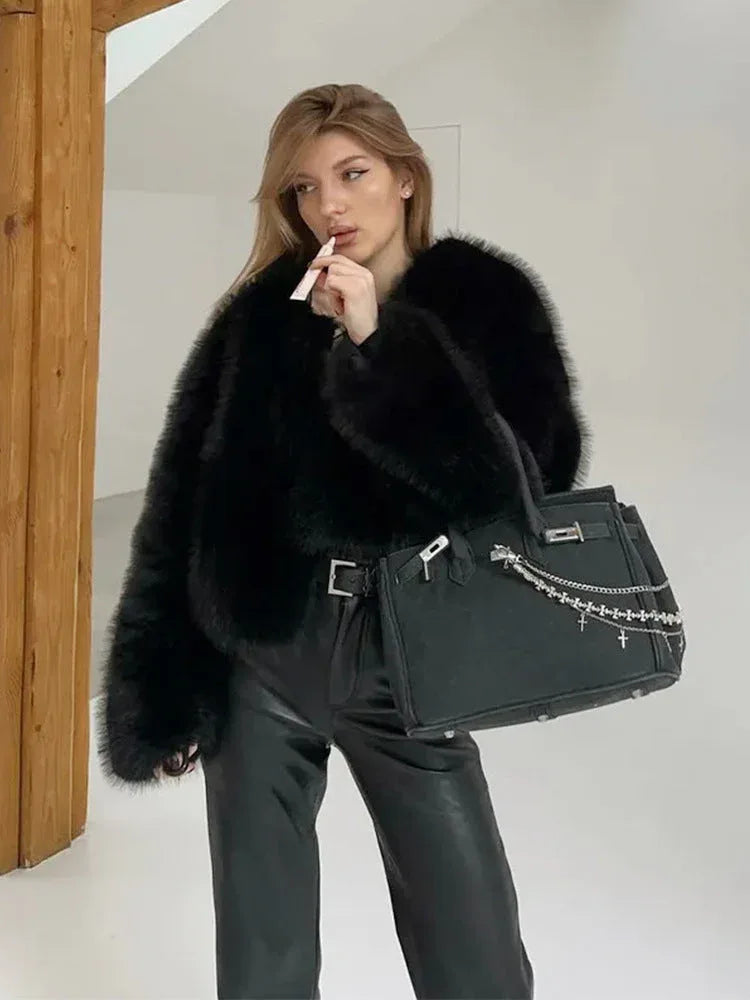 Woman wearing a black faux fur bomber jacket with leather pants and a black handbag.