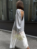 Woman from behind wearing a grey open-back knit sweater and a white skirt