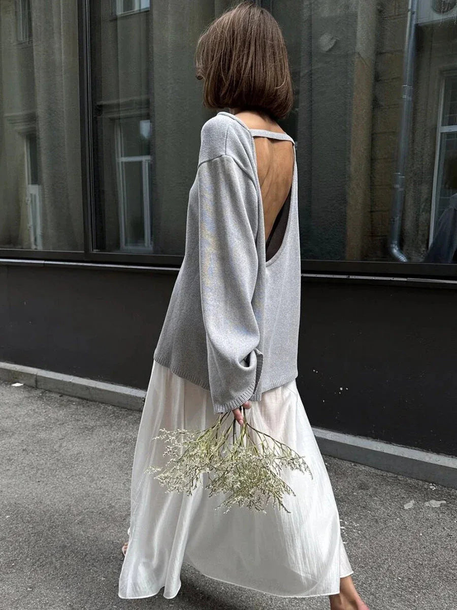 Woman from behind wearing a grey open-back knit sweater and a white skirt