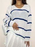 Woman wearing a white knit sweater with horizontal navy blue stripes and a v-neckline.