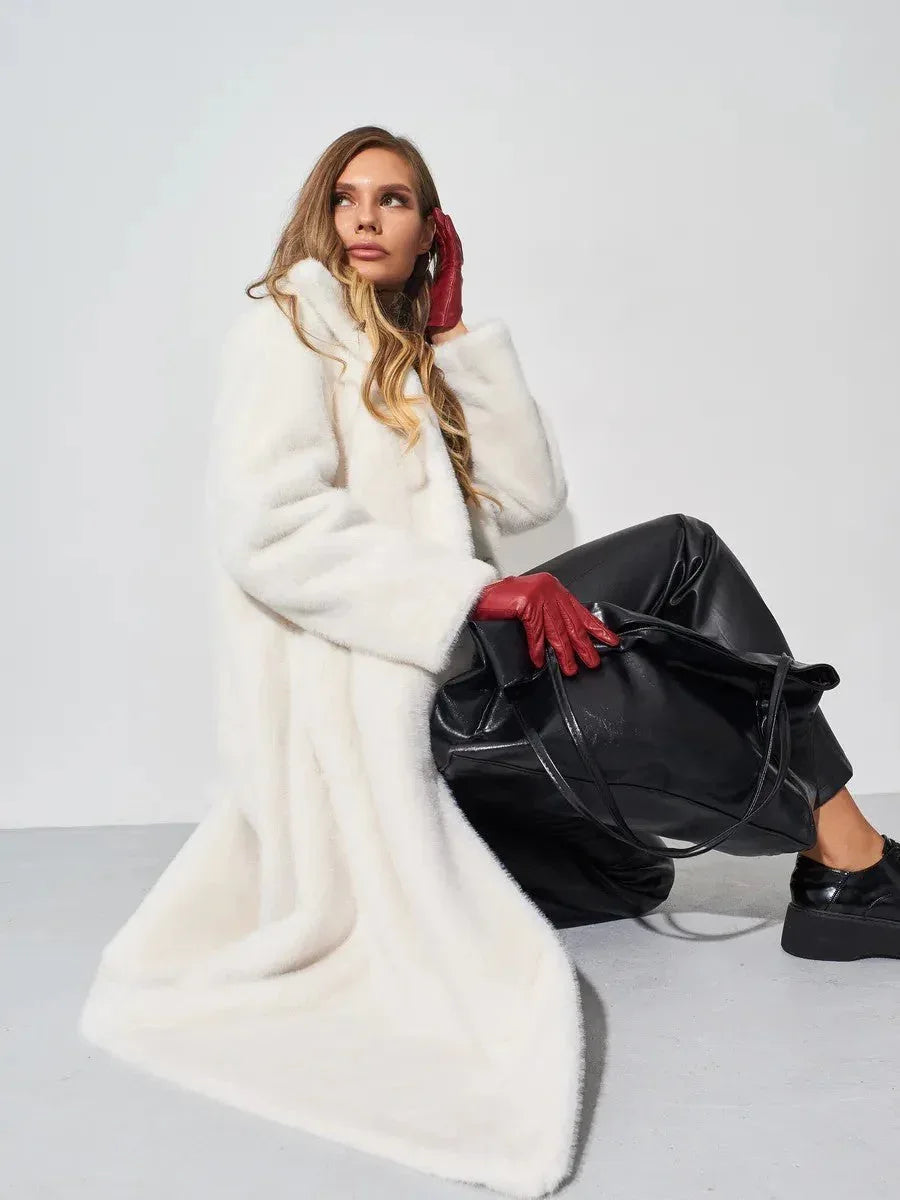 Woman sitting in a white faux fur coat with red gloves and a black handbag.