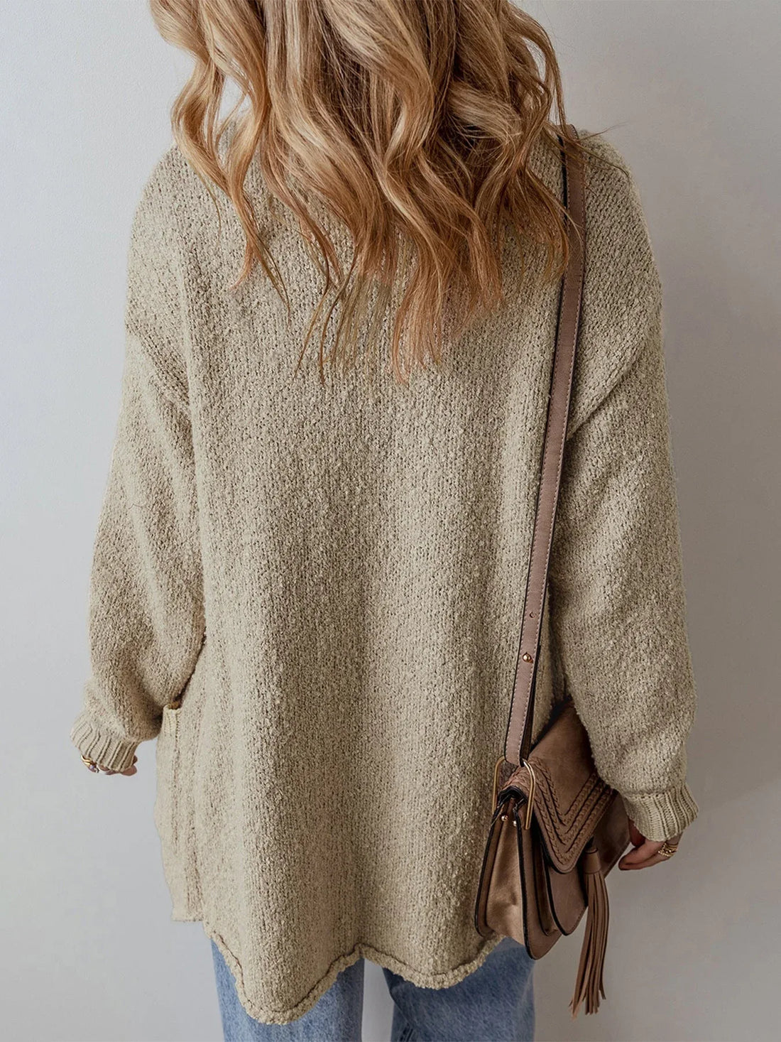 Woman wearing a longline beige textured knit cardigan with a pointed collar and button-up closure.
