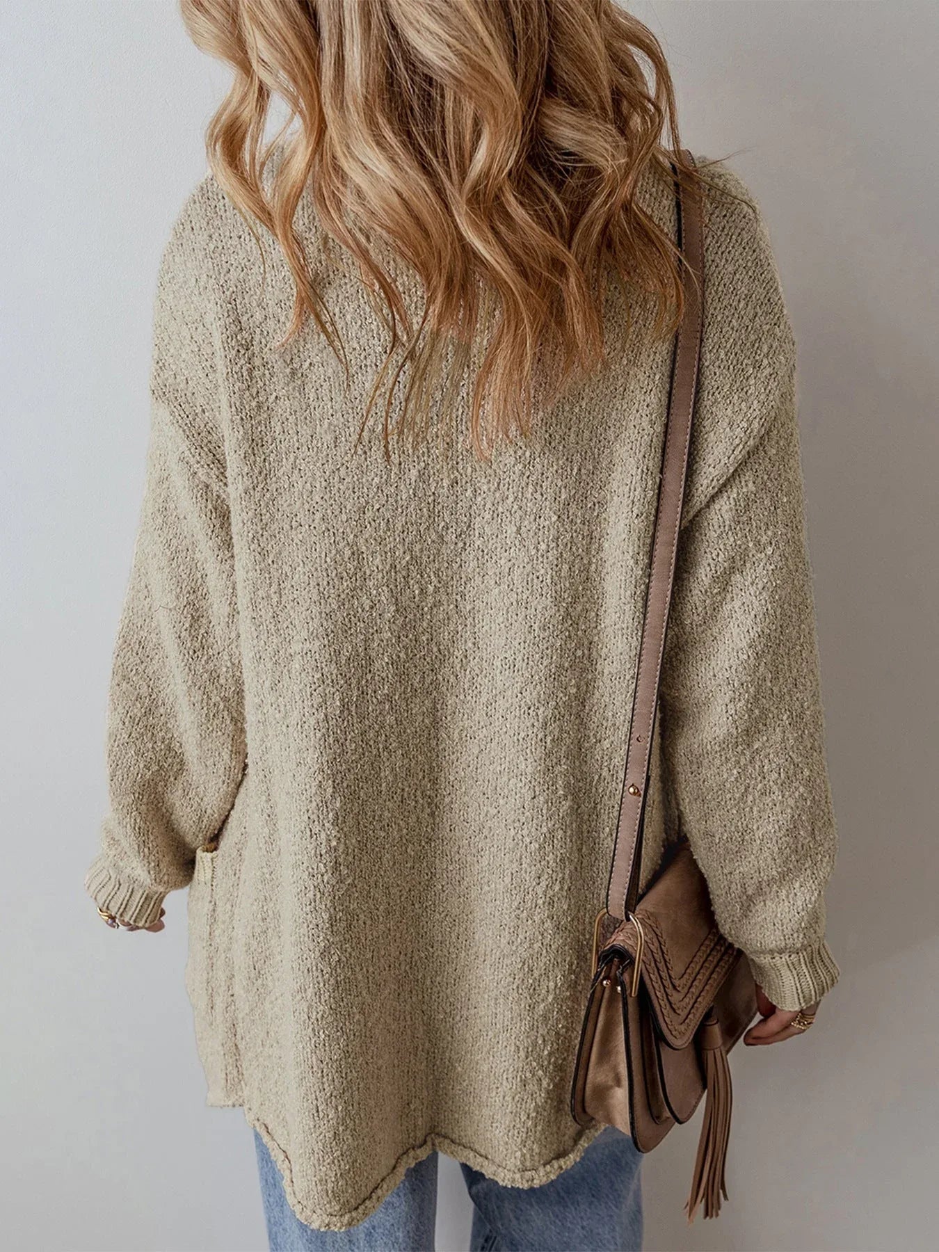 Back view of a woman wearing a longline beige textured knit cardigan with pockets.