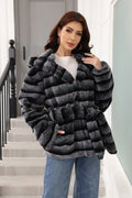 Woman posing in a hooded, belted, grey and black striped faux fur jacket, touching her hair.