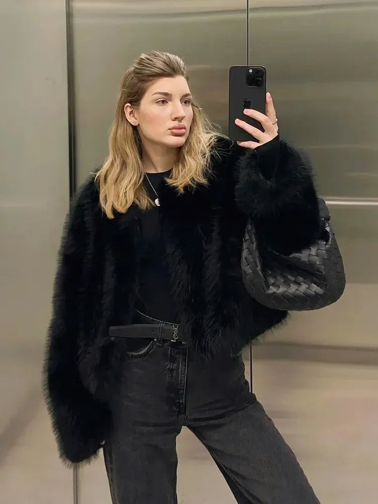 Woman taking a mirror selfie in an elevator, wearing a black faux fur bomber jacket with jeans.