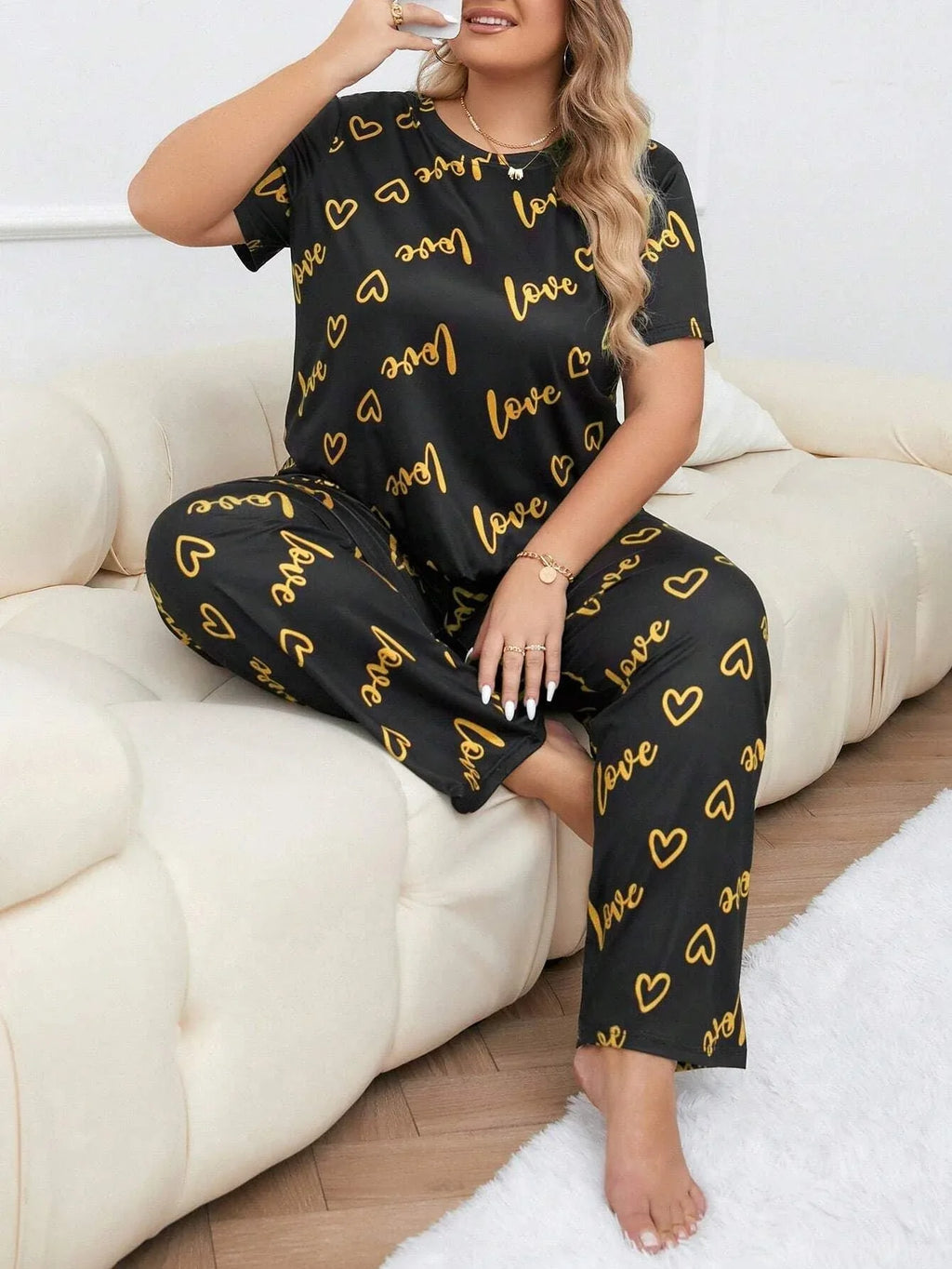 Woman wearing a black short-sleeve pajama top and pants with a gold heart and 'love' graphic print, sitting on a couch.