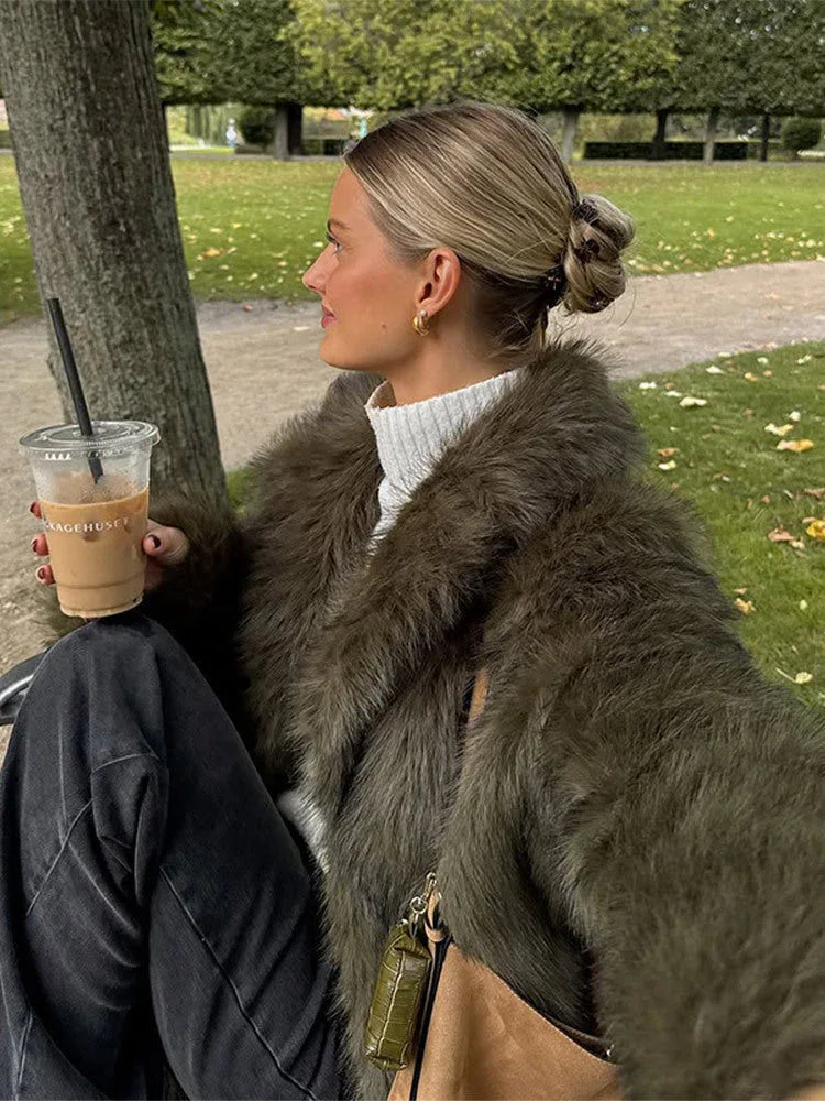 Close-up of a woman wearing a green faux fur jacket and white turtleneck, holding a coffee cup.
