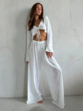 Woman wearing a white sheer knit two-piece set with a cropped tie-front top and wide-leg pants.