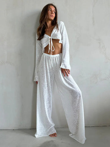 Woman wearing a white sheer knit two-piece set with a cropped tie-front top and wide-leg pants.