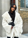 Woman wearing a white faux fur coat with a shawl collar and a belted waist.
