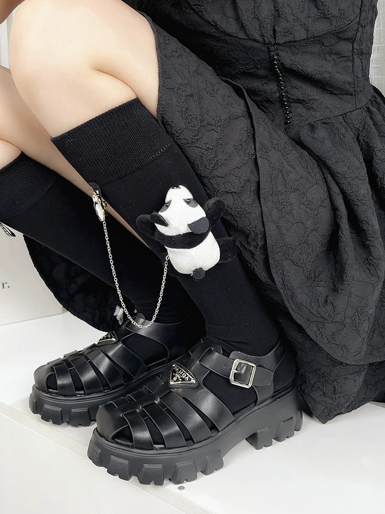 Close-up of black knee-high socks featuring a plush panda accessory attached by a silver chain.