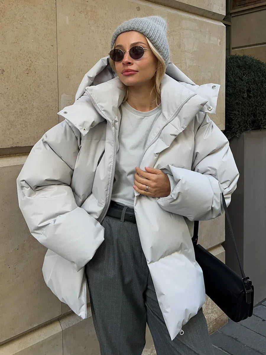 Woman in a light gray puffer jacket, gray t-shirt, gray pinstripe pants, and a gray beanie.